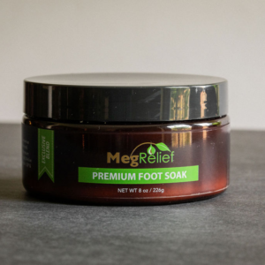 Jar of MegaRelief Premium Foot Soak with green label on dark brown container sits on a gray surface. The lid is black and glossy.